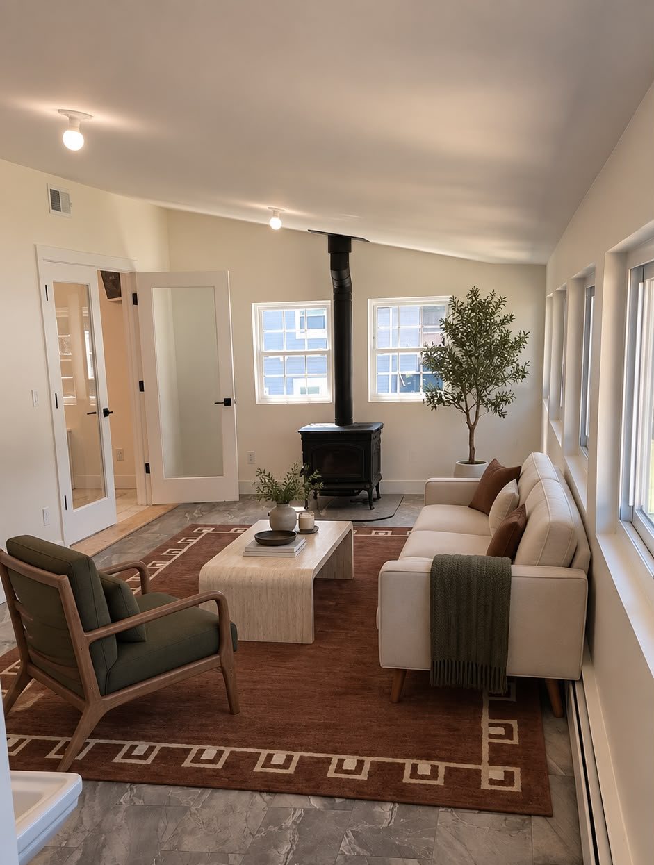 A living room staged by Stage & Decor with a cream sofa, travertine coffee table, rust rug and olive tree