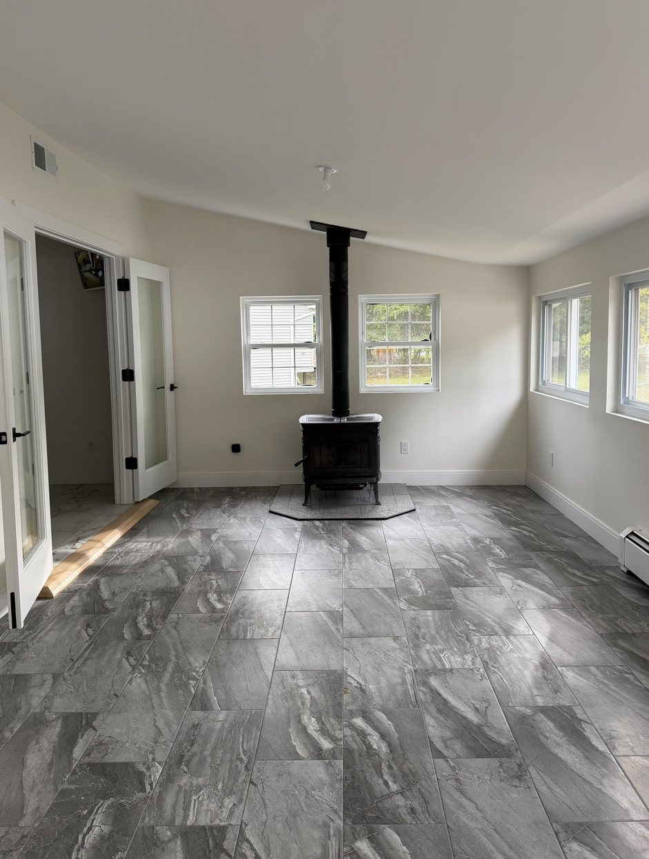 Before: an empty living room with a wood stove and bare tile floor
